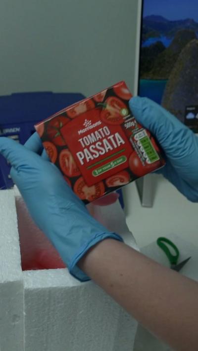 Blue gloved hands holding a packet of tomato passata