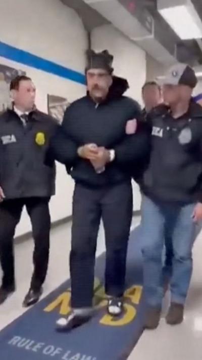 Maduro is led down a hall by two men on either side of him. 