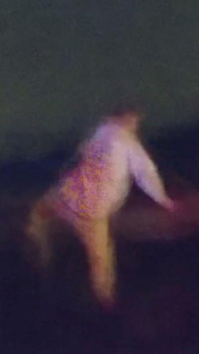 Blurry image of man in a white top and beige trousers walking away from the camera at night 