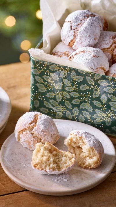 Two almond snowball biscuits, one broken in half, sit on a plate. A box with more biscuits is behind