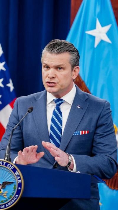 Pete Hegseth wears a light blue suit, white shirt and blue and white striped tie while speaking to the press at the Pentagon.