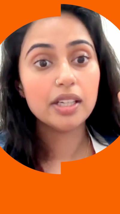 A woman with long, dark hair talks to the camera