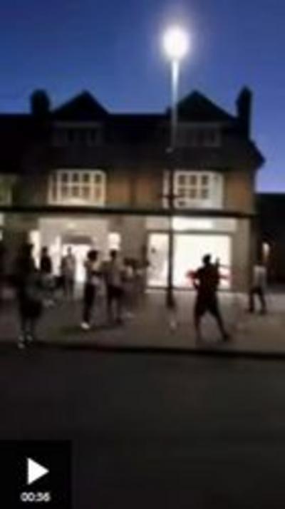 People silhouetted on a dark street in front of a lit shop window and a street lamp