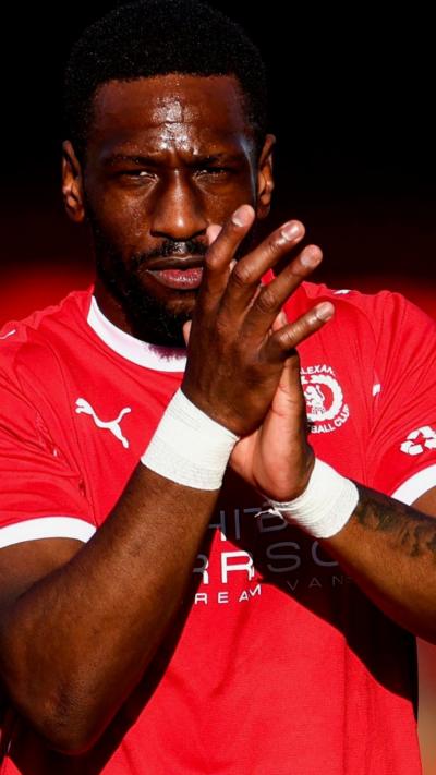 A black footballer in a red shirt applauds fans