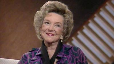 Beryl Reid sits in front of a brown background