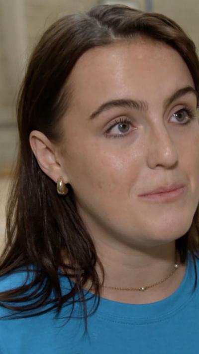 Leah is wearing a blue t-shirt, she has long brown hair