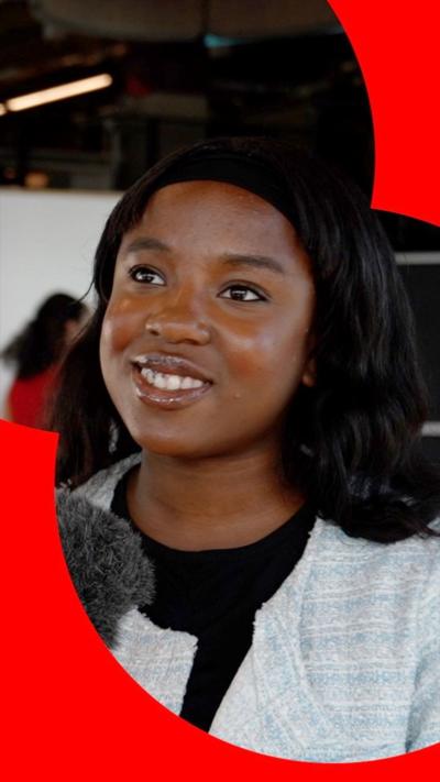 Young person being interviewed, smiling to camera in front of a microphone, with black hair.