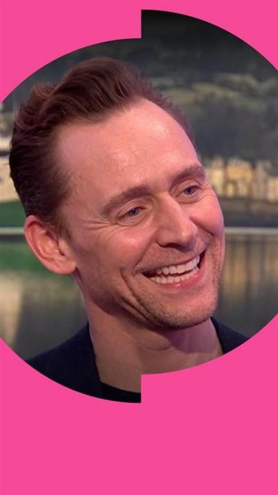 Tom Hiddleston smiles. He has swept back hair and wears a blue blazer and black T-shirt.