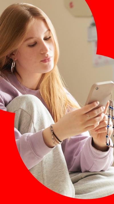 A teenager with long, blonde har sits in a bedroom looking at her phone