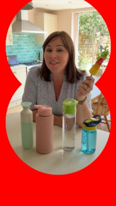 Catherine Burne holds an ice lolly in a kitchen with water bottles