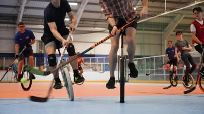 Men on unicycles playing hockey inside a sports stadium