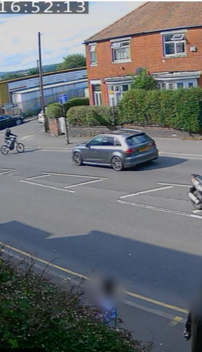 A grey audio car on a suburban street with an electric bike a few feet ahead of it facing the car