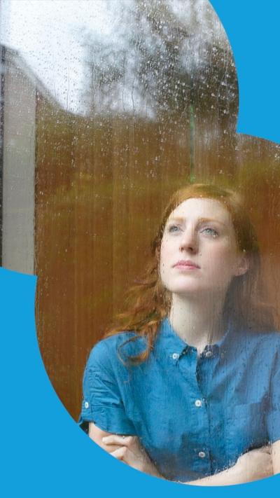 A woman looks out the widon at the rain