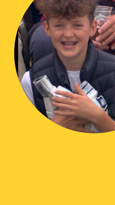 A boy smiles while holding a pair of batting gloves