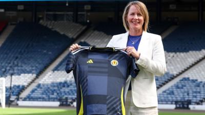 New Scotland head coach Melissa Andreatta in a white suit holding a Scotland top.