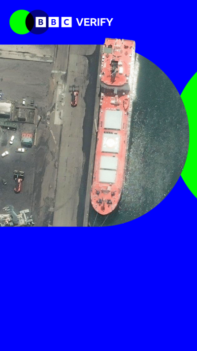 A UK boat loading cargo at a harbour. The image is imposed over the BBC Verify colours and branding