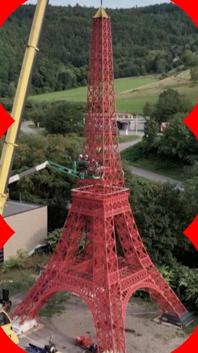 Red replica of Eiffel Tower with yellow crane next to it