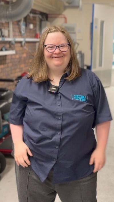 A smiling woman stands in a work uniform in a parking garage for wheelchairs.