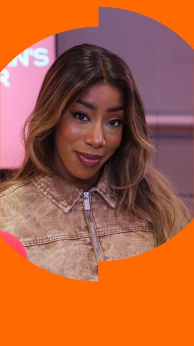 Kamille has long brown hair and is wearing a brown zipped-up jacket.