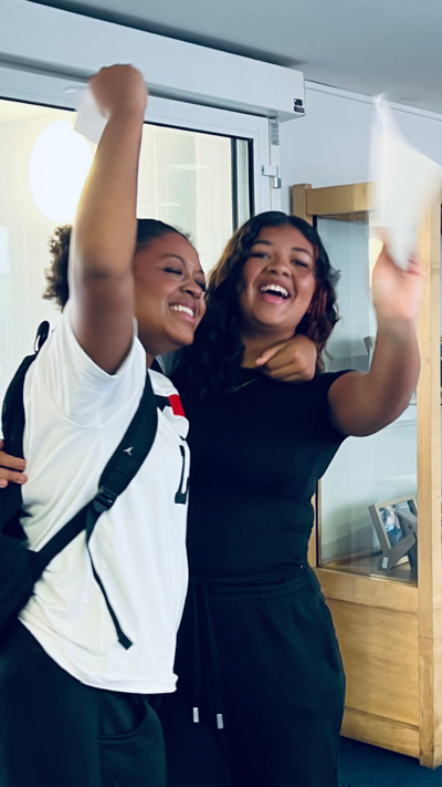 Two young women smile and embrace as they celebrate their GCSE results