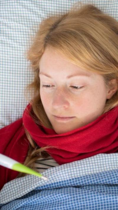 Woman wearing in bed wearing red scarf and holding thermometer 
