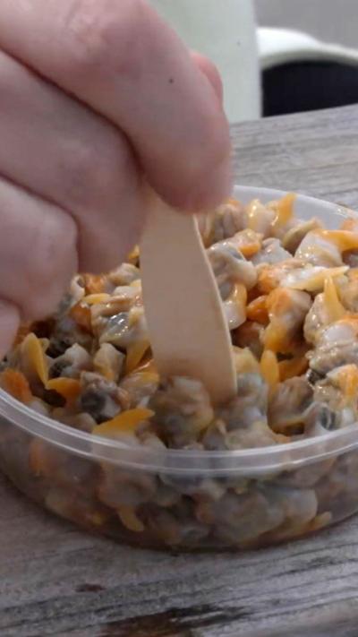 Man places wooden fork into a dish of cockles