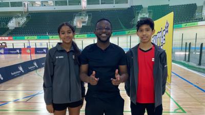 De Graft stands with two young Badminton players on the court.