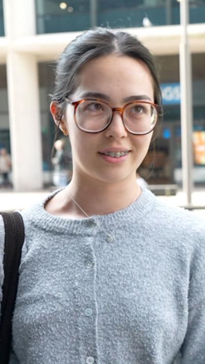 A woman with glasses and braces in a grey cardigan