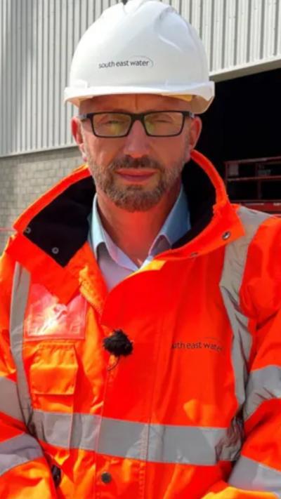 A man wearing glasses and an orange jacket looks at camera