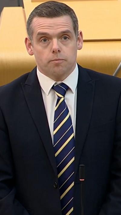 Douglas Ross standing in Holyrood chamber wearing dark suit and striped tie
