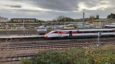 A passenger train at a platform, seen looking across the tracks.