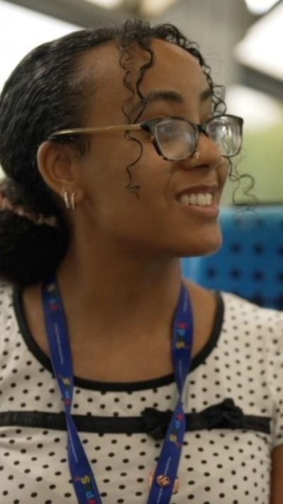 A young woman wearing glasses and a white top with black spots