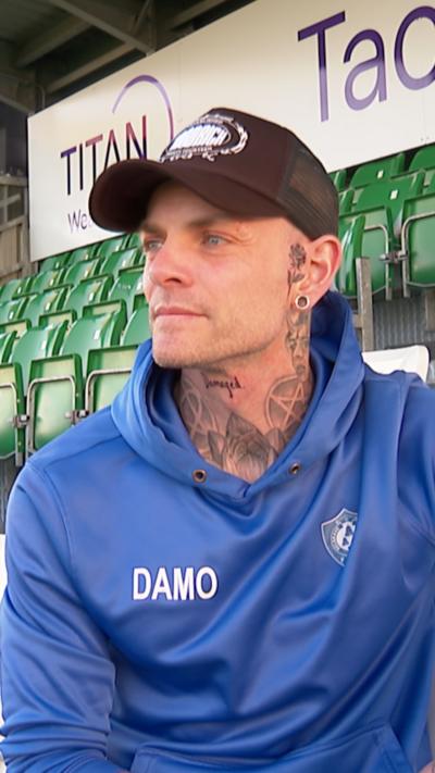 A man in a black cap and blue jumper looking off to the left of the camera