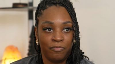 Khedidja ‘Deesh’ Teape, a black woman with braids and gold earrings looks into the camera 