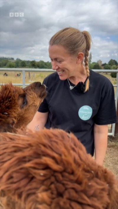 Amy Saunders smiles down at a red alpaca, who looks up at her