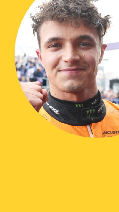 A man in an orange racing suit pumps his fist and looks at the camera