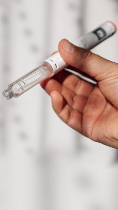 Close up of hands holding a vial containing clear liquid with its cap off.