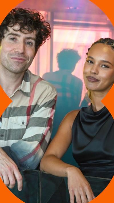 Nick Grimshaw in a checked shirt standing beside Alisha Boe, in black top leaning over bannister