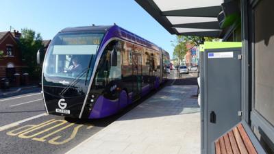 A Glider bus at a bus stop.