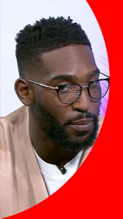 Tinie Tempah has short dark hair and is wearing a beige quarter-zip jumper.