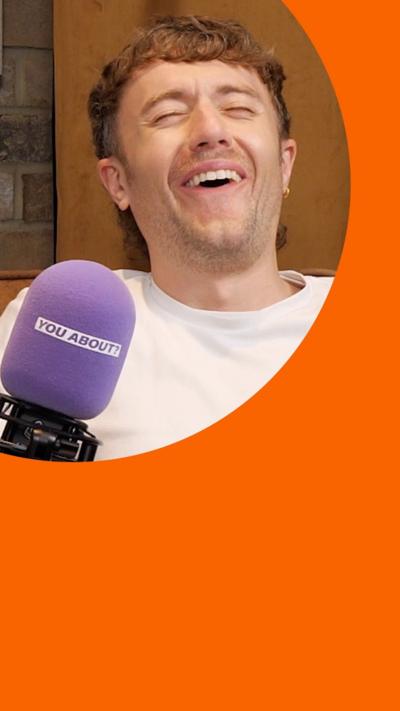 Roman Kemp sat on chair in front of a purple microphone and laughing