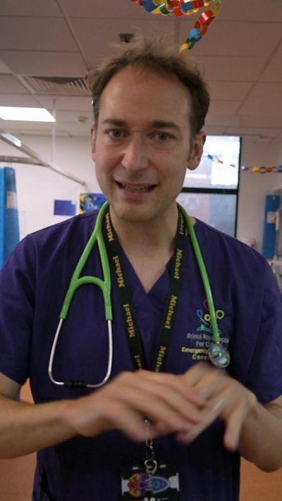 A doctor wears blue scrubs and has a green stethoscope. 