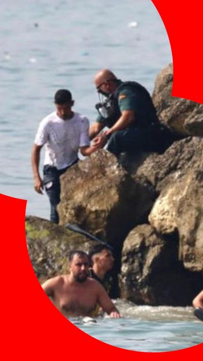 Men swimming as police officer standing on rocks holds arm of man in white t-shirt