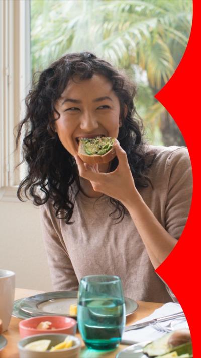A woman smiles while eating avocado on toast