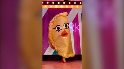 A drag queen, dressed as a calzone with eyes and lips, walks into the RuPaul's Drag Race UK werk room