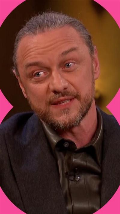 James McAvoy has greying hair tied back, and a beard and moustache. He is wearing a shiny black shirt and a black jacket