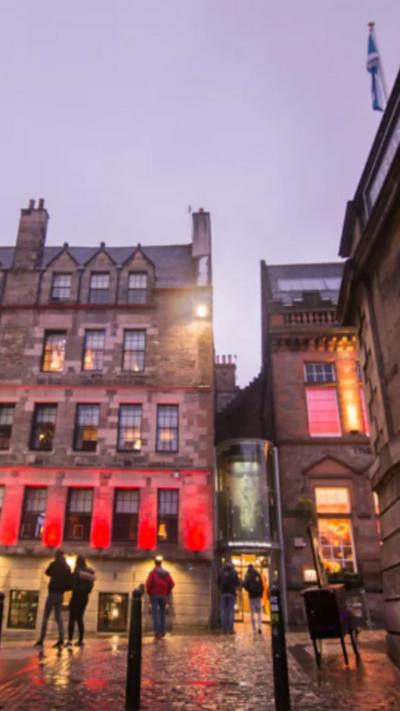 Edinburgh city centre street at night with lit up buildings and a few people walking about.