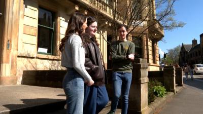 Triùir oileanaich nan seasamh còmhla air an t-sràid an Glaschu agus iad a' còmhradh ri càch a chèile. 