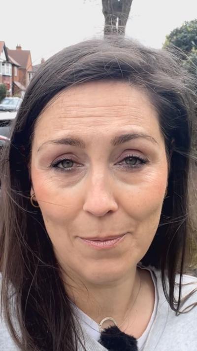 A woman with dark hair in a street looking into a camera