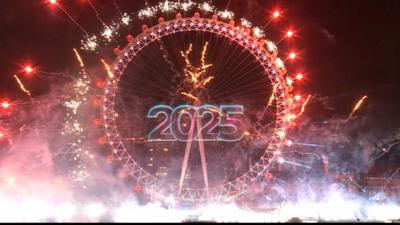 The London Eye with fireworks shooting off it. In the middle is a projection of the number 2025